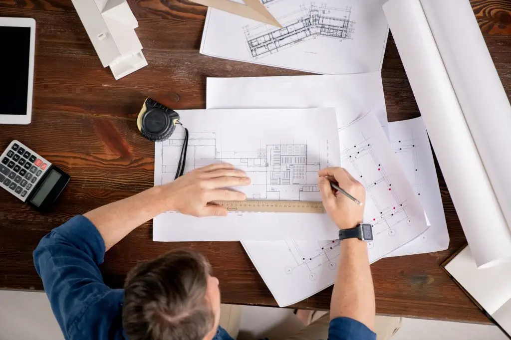 Overview of contemporary engineer sitting by table and correcting sketches